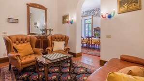 Uma sala de estar com poltronas de couro, um tabuleiro de xadrez, um espelho e um espaço de refeições com mesa e cadeiras.