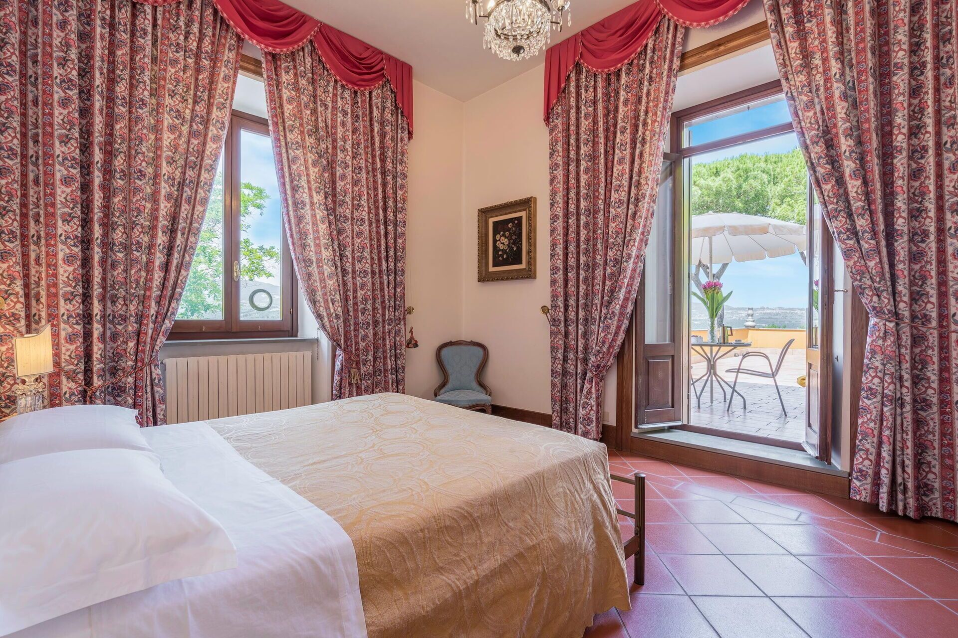 A hotel room with a bed, a chair, a table with an umbrella, and a view of the outdoors.