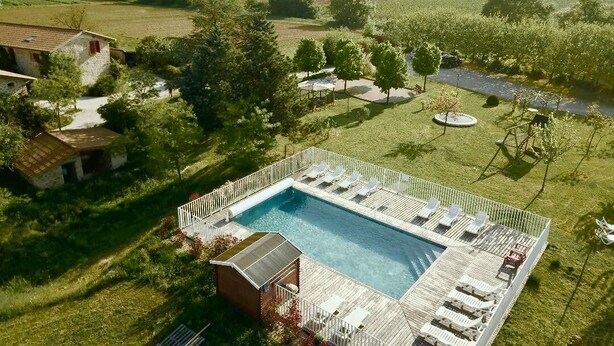 A pool with a wooden deck and lounge chairs, surrounded by a grassy area with trees and a view of distant hills. - Ferienwohnung mit Beheizten Pool bis 5 Personen (Marsaz)