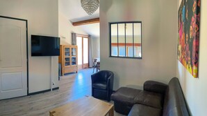 A living room with a sofa, a coffee table, a TV, a cabinet, and a window with blinds. - Ferienwohnung mit Beheizten Pool bis 5 Personen (Marsaz)