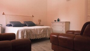 A bedroom with a bed, two pillows, a nightstand, a dresser, and two brown leather chairs.