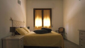A bedroom with a bed, nightstands, a chair, and a window with curtains.
