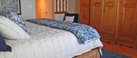 A bedroom with a large bed, a wooden wardrobe, and a door leading to another room.