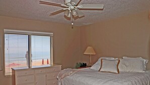A bedroom with a bed, a dresser, a ceiling fan, and a window with blinds. - Second floor three bedroom three bath direct oceanfront (New Smyrna Beach)