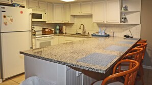 A kitchen with white cabinets, a granite countertop, a refrigerator, a microwave, and a sink. - Second floor three bedroom three bath direct oceanfront (New Smyrna Beach)