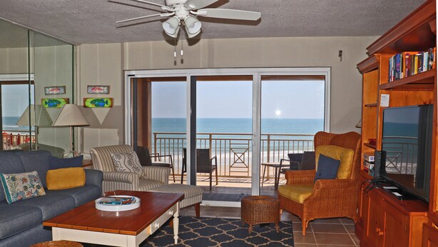 A living room with a sofa, armchairs, a coffee table, and a bookshelf. There is a view of the ocean through a sliding glass door. - Second floor three bedroom three bath direct oceanfront (New Smyrna Beach)