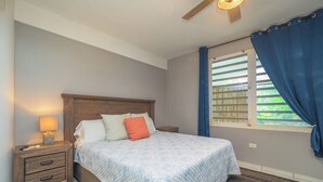 Una camera da letto con una testiera in legno, un letto con copriletto trapuntato, un comodino con una lampada e una finestra con tende blu.