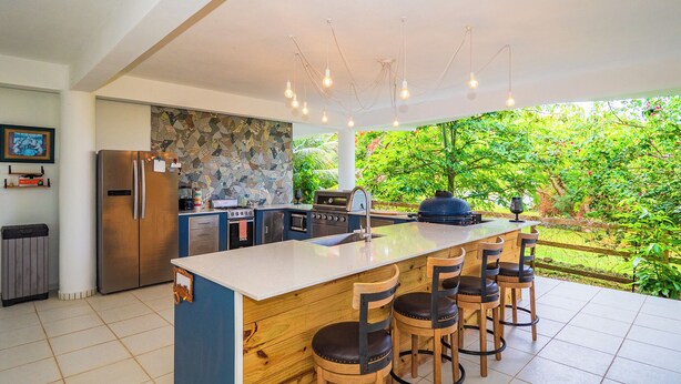 Una cucina moderna con una grande isola, sgabelli da bar e vista su un giardino rigoglioso.