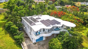 Un edificio moderno con pannelli solari sul tetto, immerso nel verde lussureggiante e nella vegetazione tropicale.