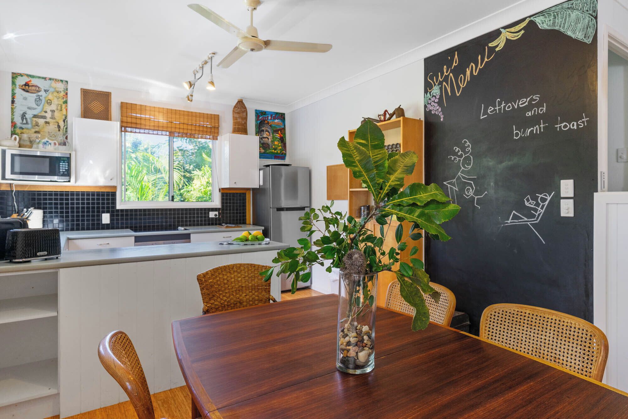 Een moderne keuken met een eethoek, met een krijtbordmenu, een plafondventilator en een groot raam met uitzicht op groen.