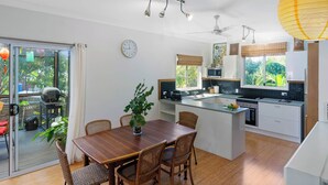 A modern kitchen with a central island, white cabinetry, and a view of greenery outside. - Enchanted Garden Island Cottage with Bikes and Air Con. (Russell Island)
