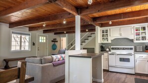 A spacious living area with a wooden ceiling, a kitchen with white cabinets, and a gray sofa. - The Lake House  - Beachfront w/ Hot tub available! (Arnold)