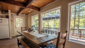 A wooden dining table with benches, large windows with a view of a deck, and a white refrigerator. - The Lake House  - Beachfront w/ Hot tub available! (Arnold)