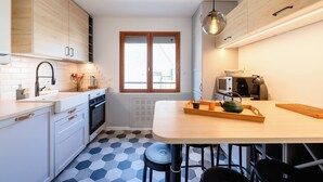 A modern kitchen with white cabinets, a wooden countertop, a large window, and a dining area with stools.