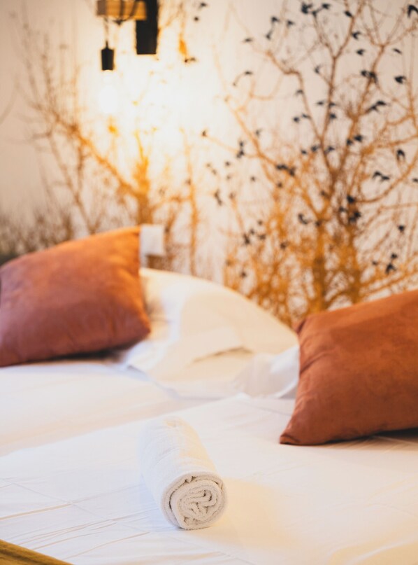 Una cama con sábanas blancas, dos almohadas marrones y una toalla blanca enrollada.