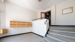 A hallway with a staircase, wooden mailboxes, and a bulletin board on the wall.