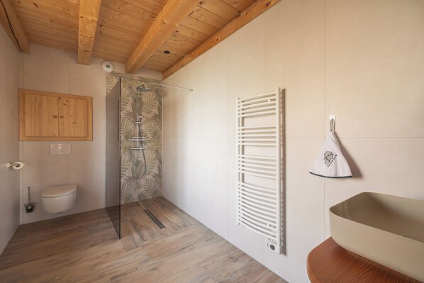 Un baño moderno con techo de madera, cabina de ducha de vidrio, inodoro blanco y toallero con una toalla decorativa.