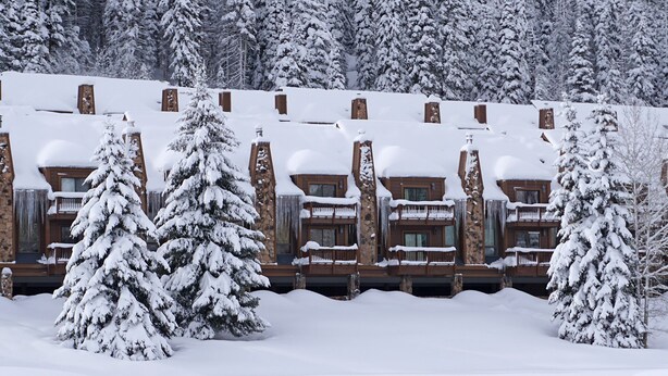 Een met sneeuw bedekte lodge met meerdere balkons en een stenen gevel.
