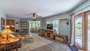 A spacious living room with a sofa, coffee table, and TV, a dining area with chairs, and a kitchen with wooden cabinets. - Hike Inn Bryson-Game Room - Fire Pit - Private Location -Wrap Around Deck (Bryson City)