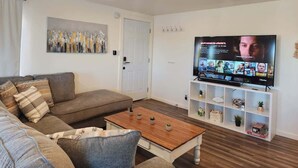 Un salon comprenant un canapé, une table basse, un téléviseur et une étagère ornée d’objets décoratifs.