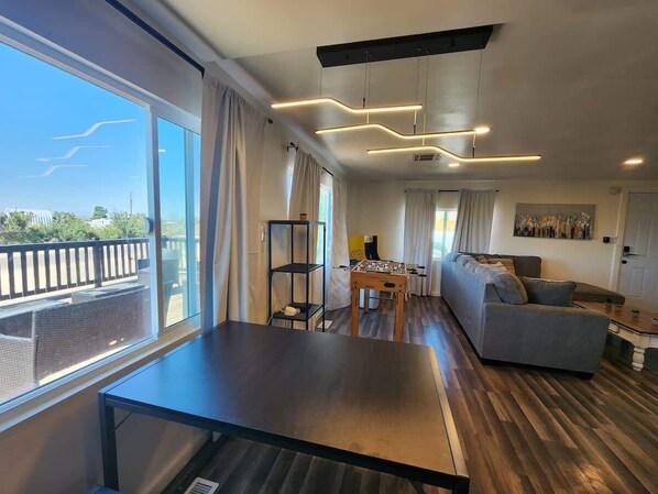 Una sala moderna con un sofá, una mesa de centro y una mesa de futbolín. Una ventana grande ofrece vistas al exterior.