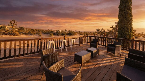 Une terrasse en bois, meublée de meubles en osier, offrant une vue sur le paysage désertique.