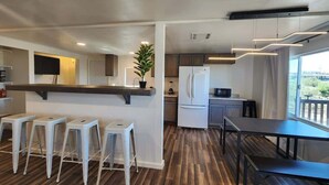 Une cuisine moderne avec un plancher en bois, des tabourets de bar blancs, un réfrigérateur et une table à manger.