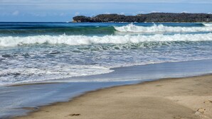 Una playa con olas, una orilla arenosa y un promontorio rocoso a lo lejos.
