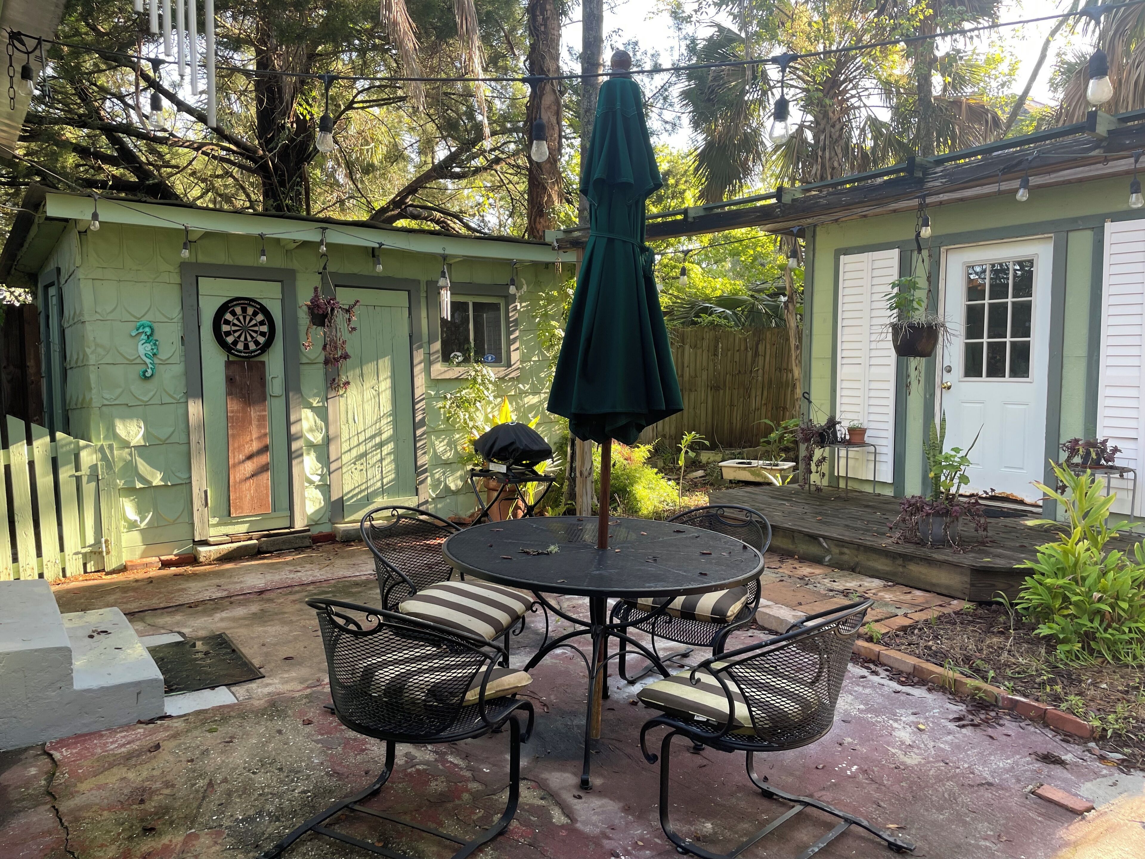 Un patio con una mesa redonda y cuatro sillas, rodeado de vegetación y una valla de madera.