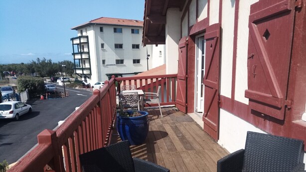 Een balkon met rieten stoelen, een potplant en uitzicht op een parkeerplaats en gebouwen.
