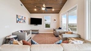 A spacious living room with a ceiling fan, a flat-screen TV, and a large window offering a view of the ocean. - Beachfront Home w/ Private Boardwalk (Port St. Joe)