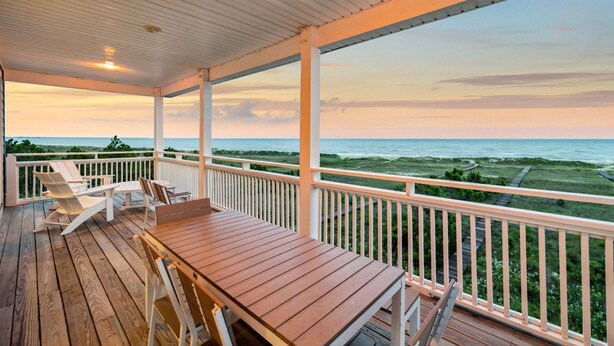 A covered deck with a wooden table and chairs, overlooking a beach with a view of the ocean and distant shoreline. - Beachfront Home w/ Private Boardwalk (Port St. Joe)
