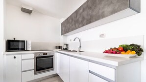 Une cuisine moderne avec des meubles blancs, un four à micro-ondes encastré, un four classique et un évier en acier inoxydable.