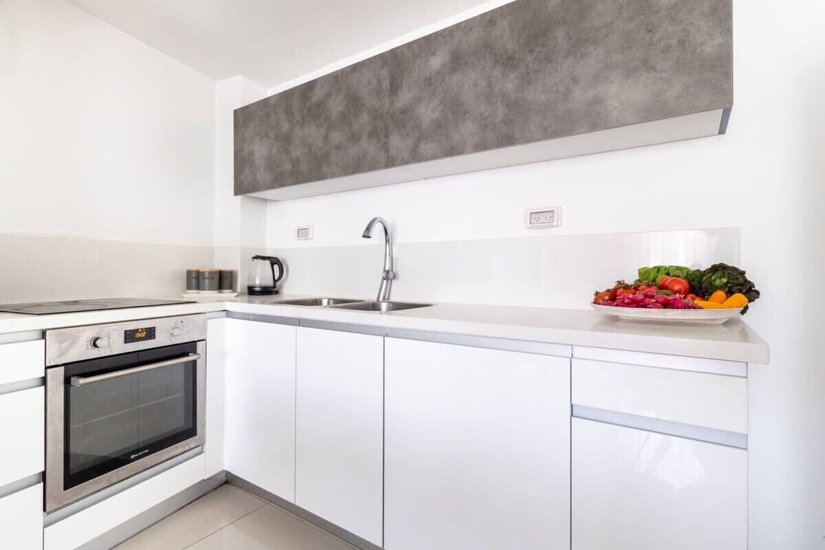 Cozinha moderna com armários brancos, forno embutido, pia de aço inoxidável e backsplash cinza.