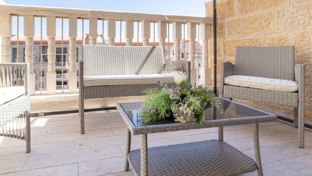 Un balcon agrémenté de meubles en osier, d’une table en verre et d’une plante en pot.