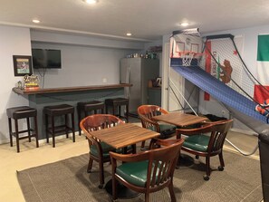 Uma área de bar com banquetas, um balcão e um mural com um cesto de basquete.