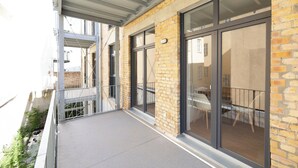 A balcony with a metal railing, brick walls, and large glass doors leading to an interior space with a table and chairs. - ★ Ko-Living - Gaming Suite | In the center | Up to 6 people | Arcade ★ (Halle (Saale))