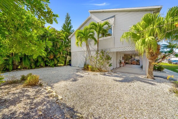 Une maison moderne à l’extérieur blanc, entourée d’une végétation luxuriante et de palmiers.