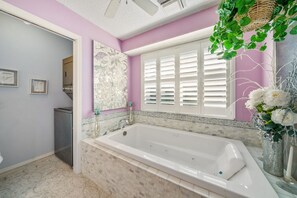 Une salle de bain avec une grande baignoire, une fenêtre avec des volets blancs et un miroir décoratif.