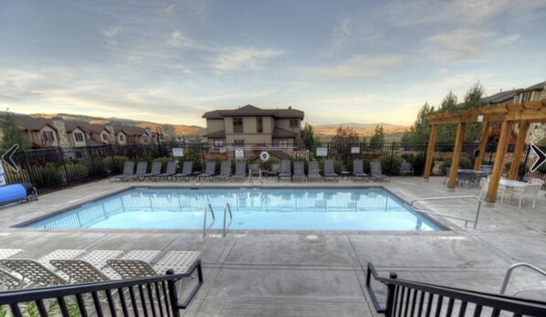 A rectangular swimming pool with lounge chairs and a pergola on a patio.