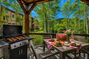 An outdoor patio with a grill, picnic table, and a view of a forested area.
