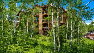 A multi-story log cabin with a balcony, surrounded by dense greenery and trees.