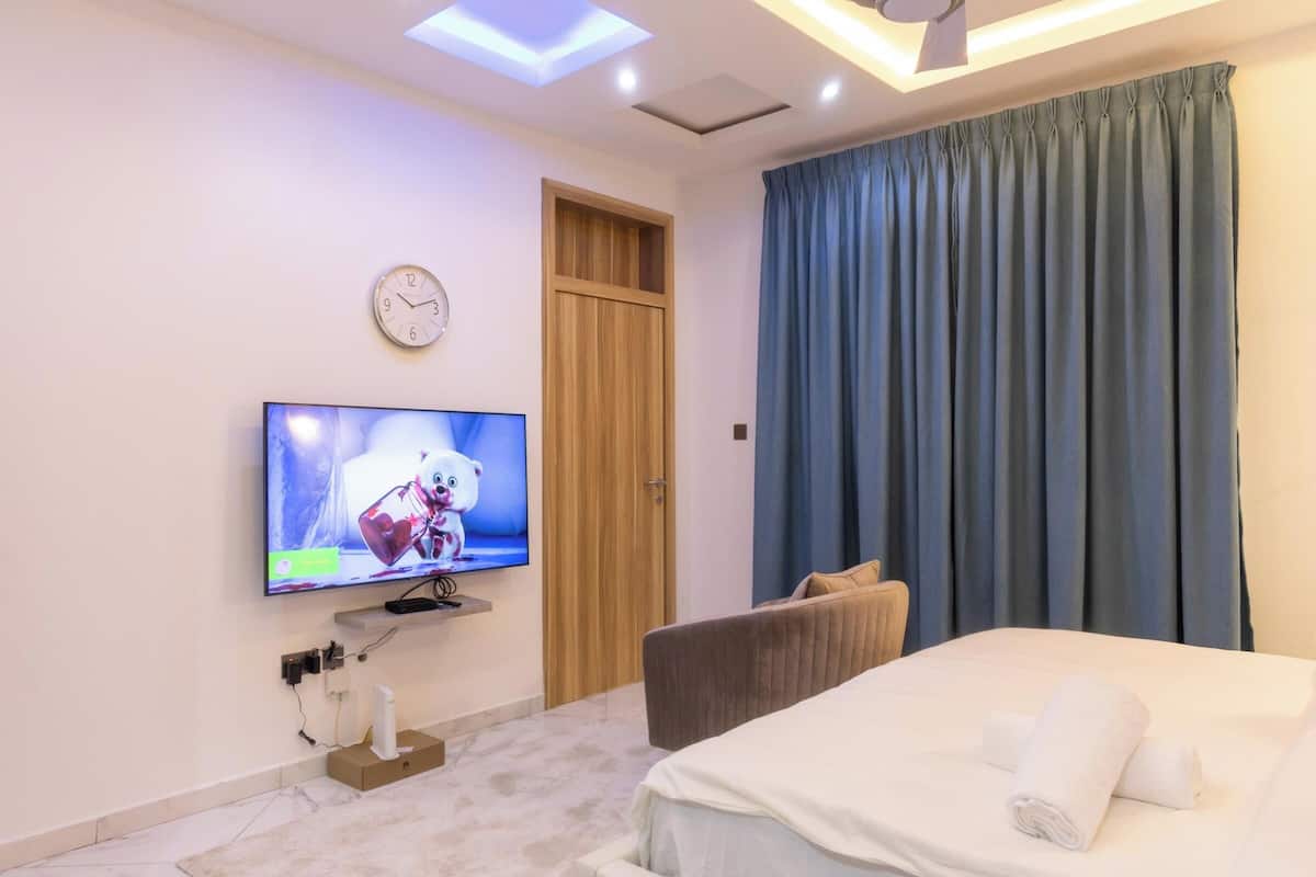 Une chambre d’hôtel avec un lit, un téléviseur fixé au mur, une porte en bois et un rideau bleu.