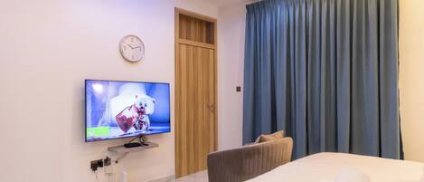 A hotel room with a bed, a TV on the wall, a wooden door, and a blue curtain.