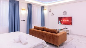 A modern hotel room with a bed, a sofa, a TV, and a ceiling fan. - Akafia's Court (Accra)