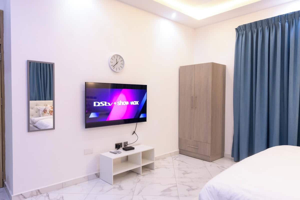 Une chambre d’hôtel moderne équipée d’un téléviseur à écran plat, d’une armoire en bois, d’un lit et d’une petite table console blanche.