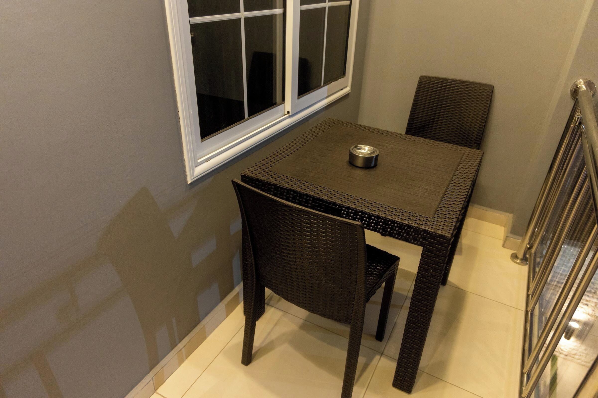 A small dining area with a table and two chairs, a window, and a metal railing.