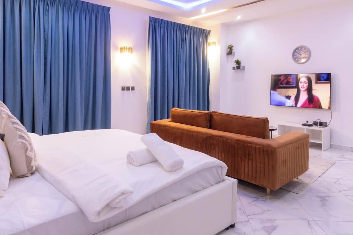 Une chambre d’hôtel moderne avec un grand lit, un canapé marron, un téléviseur à écran plat et des rideaux bleus.
