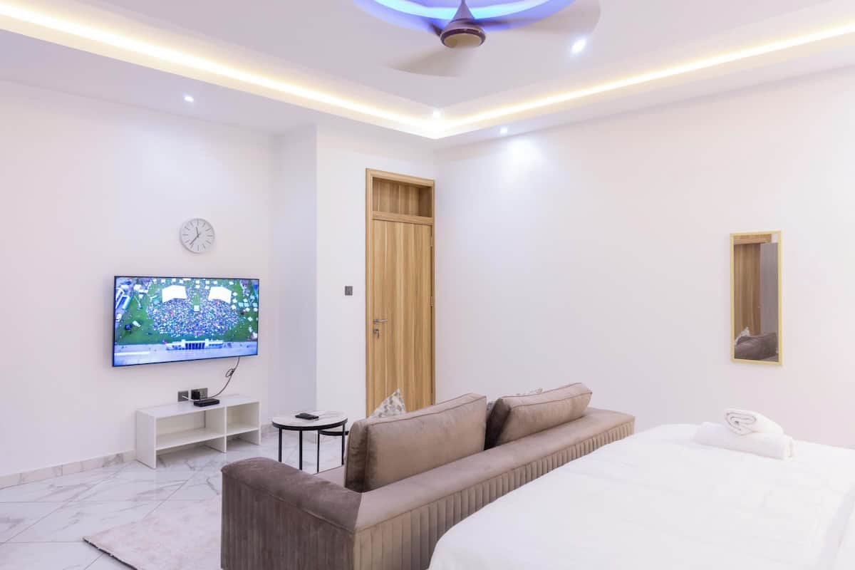 Une chambre d’hôtel moderne avec un grand lit, un canapé, un téléviseur fixé au mur et un ventilateur de plafond.