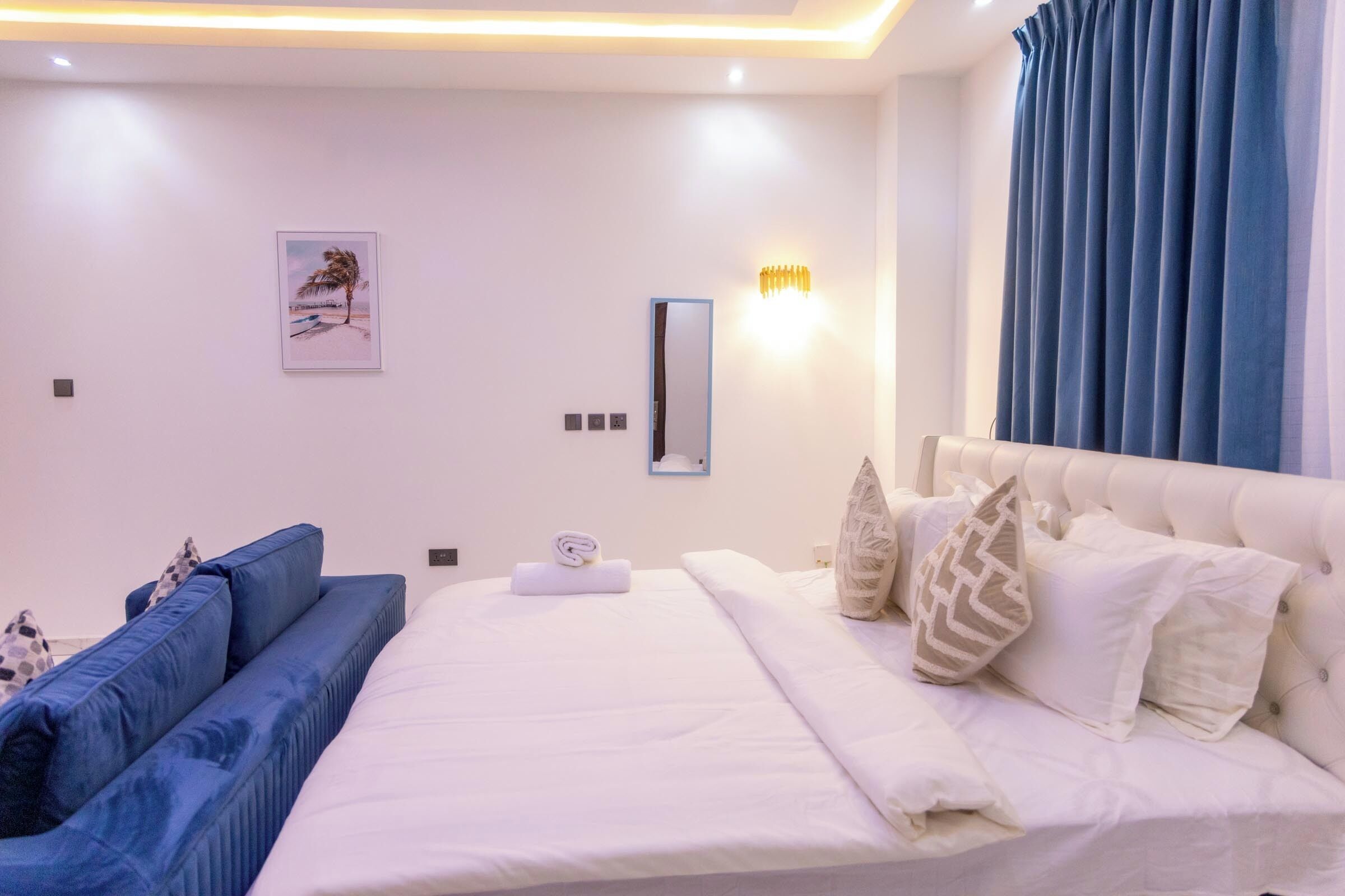 A modern bedroom with a large bed, a blue sofa, and a wall-mounted mirror.
